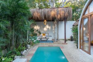 a pool in the backyard of a house with a thatched roof at Villa Sanah in Tulum
