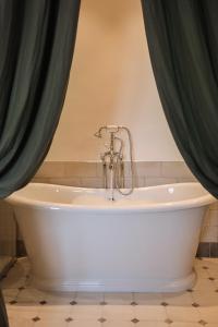 a white tub in a bathroom with green curtains at L'Abbaye Hôtel in La Colle-sur-Loup