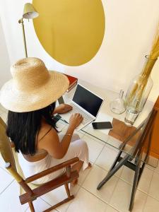 una mujer con un sombrero de paja sentada en un escritorio con un portátil en Casa de praia no Flamengo en Salvador