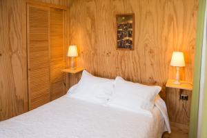 1 dormitorio con 1 cama blanca y 2 lámparas en Del Pescador Hotel Cabañas en Frutillar