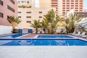 une piscine avec des chaises et un bâtiment dans l'établissement Flat Top - 100 M Da Praia De Pitangueiras 4083, à Guarujá
