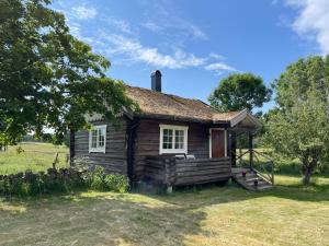 uma antiga casa de madeira com um alpendre num campo em Backgårdens Timmerstuga em Falköping