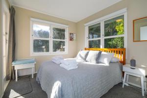 a bedroom with a large bed with two windows at The Greenkeeper's Cottage in Rotorua