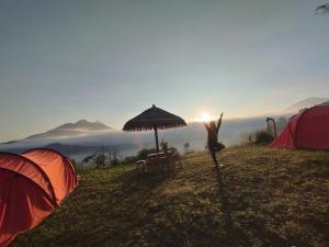 a person standing on a hill with their arms in the air next to tents at Kintamani Adventures 'Life Hurt, Nature Heal' in Kintamani