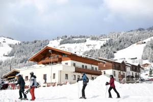 quatro pessoas em esquis na neve em frente a um alojamento de turismo selvagem em Appartements neben der Gondelbahn - Haus Nord em Brixen im Thale