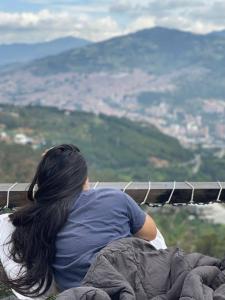 una mujer sentada en una cornisa mirando las montañas en Glamping ecoglam Medellín, en Copacabana