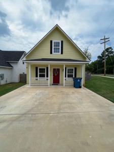 a yellow house with a red door on a driveway at ComfyStay in Gladewater