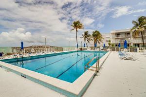 a pool with chairs and palm trees and a building at Ocean-View Key Colony Beach Condo with Pool Access! in Key Colony Beach