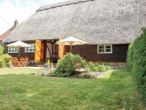 a house with a thatched roof with an umbrella at Wren Cottage in Canterbury