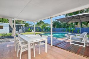 une table et des chaises blanches ainsi qu'un parasol sur la terrasse dans l'établissement Endeavour Holiday House Clifton Beach, à Clifton Beach