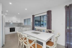 a white kitchen with a white table and chairs at Endeavour Holiday House Clifton Beach in Clifton Beach
