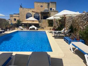 a swimming pool with chairs and umbrellas next to a building at Botanica B&B in Xagħra