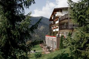 a building on a hill with trees in the foreground at Bella Vista Hotel Emma in San Vigilio Di Marebbe