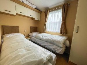 een kleine slaapkamer met 2 bedden en een raam bij Lovely Caravan By The Beach In Pakefield, Suffolk Ref 68007cl in Lowestoft