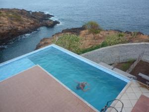 a person in a swimming pool next to the ocean at Villa Halcyon cabo verde in Cidade Velha