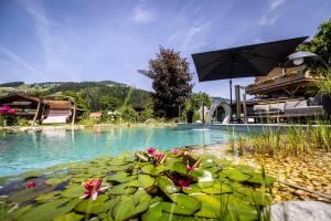 a pool with an umbrella and lilies in the water at Landhaus Rustika in Wagrain +183 photos