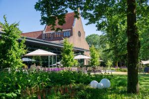 um edifício com mesas e guarda-sóis num parque em Hotel Kontakt der Kontinenten em Soesterberg