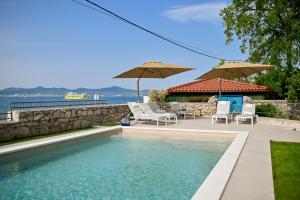 a swimming pool with chairs and umbrellas next to the water at Villa Hrešć I in Zadar