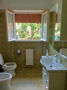 uma casa de banho com um lavatório, um WC e uma janela. em appartamento con giardino vicino al mare em Palidoro