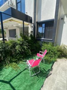Deux chaises roses assises sur l'herbe à l'extérieur d'une maison dans l'établissement Seaside retreat. two room apartment. quiet area, à Năvodari