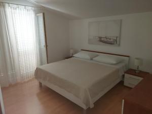 a white bedroom with a bed and two windows at Apartments Prgin in Primošten