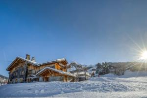 Una cabaña de madera en la nieve con el sol detrás. en Le Vieux Chalet, en La Clusaz