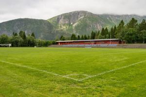 a soccer field with a building and mountains in the background at Mosjøen Apartments in Mosjøen