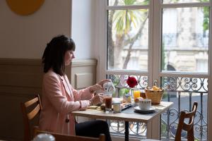 a woman sitting at a table with a cup of coffee at Hôtel & Espace Bien-être La Maison du Lierre in Biarritz