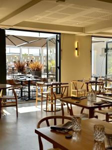 un restaurante con mesas y sillas de madera y ventanas en Logis Hôtel & Restaurant Le Vert Bocage en Franqueville-Saint-Pierre