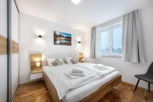 a white bedroom with a large bed and a chair at Chic Apartments with Finnish Sauna and Jacuzzi in Kranjska Gora