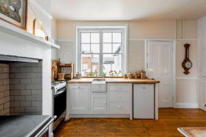 a kitchen with white cabinets and a sink and a window at Cliff-top Coastguard's Cottage, an Off-Grid Escape in Weybourne