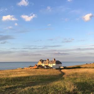 a house in a field next to the ocean at Cliff-top Coastguard's Cottage, an Off-Grid Escape in Weybourne