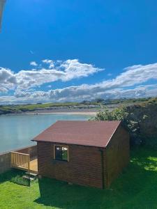 a small building with a deck next to a body of water at Cosy Portmor Log Cabin in Malin Head