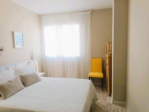 a bedroom with a white bed and a yellow chair at Villa Service - Torre Barot 5º in Calafell