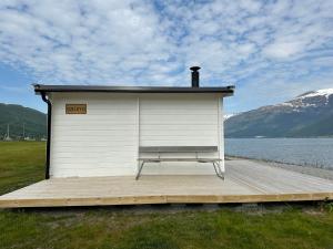 a building with a bench on a dock next to a body of water at Løkvollstranda camping As in Samuelsberg