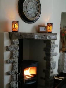 a clock on the wall above a fireplace with a fire at The Beautiful Bobbin - Premium Place to stay - Cottage with views, local walks & pubs in Tideswell