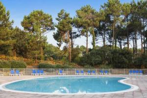 a swimming pool with blue chairs and trees at Petite Villa La Pantoufle au Domaine du Golf de Pinsolle in Soustons