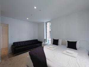 a bedroom with a large white bed and a black couch at Fully Serviced One Bed Apartment in Royal Wharf in London