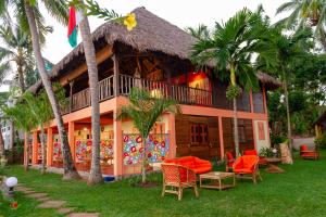 una casa con techo de paja, sillas y palmeras en La Plage de Le Zahir, en Nosy Be