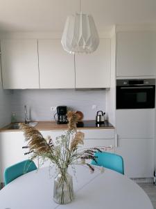 a white kitchen with a table and a vase with flowers at La Naturelle Duplex 90 in Wimereux