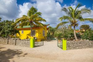 ein gelbes Haus mit einem Zaun und Palmen in der Unterkunft 26 Casa Chibi Chibi in Kralendijk