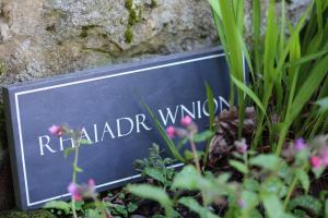 a sign in a garden with some flowers at Afon Rhaiadr Country House in Dolgellau