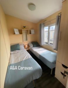 Duas camas num pequeno quarto com uma janela em A&A Caravan Holidays em Leysdown-on-Sea