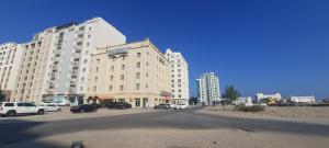 a large building with cars parked in a parking lot at Savoy Inn Hotel Apartments in Muscat