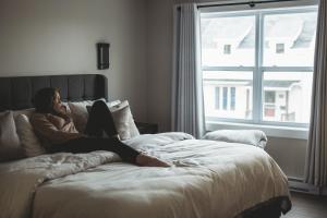 a woman sitting on a bed looking out a window at Riverside Suites in Grand Falls -Windsor