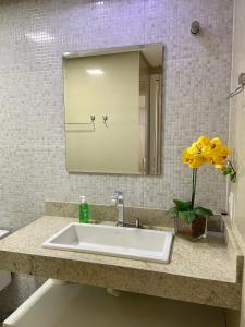 um lavatório de casa de banho com um espelho e um vaso de flores amarelas em Apartamento confortável com uma bela vista - lagoa seca Juazeiro em Juazeiro do Norte
