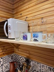 a shelf with cups and glasses and a microwave at Romantique chalet avec sauna et jacuzzi extérieur in Arthon
