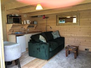 a living room with a green couch and a kitchen at Cosy Garden Log Cabin in Salisbury