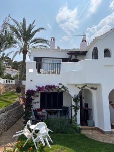 una casa bianca con due sedie bianche in cortile di Playa Son Bou, Menorca a Son Bou