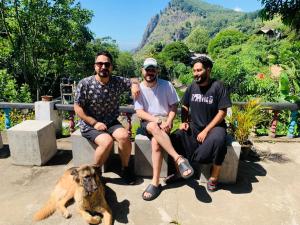 three men sitting on a bench with a dog at Rock View Hostel Ella in Ella